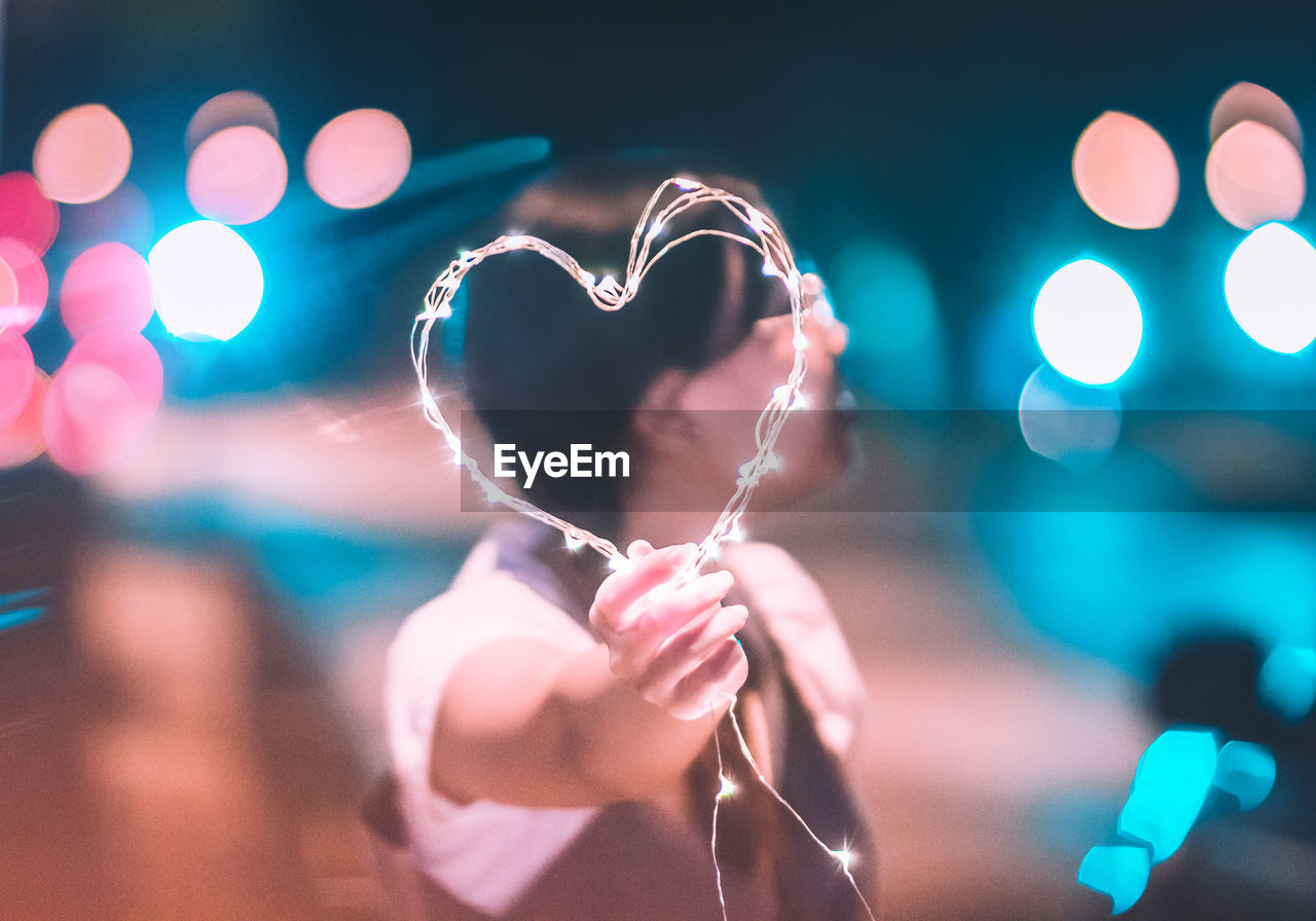 Man holding illuminated heart shape while standing on road at night