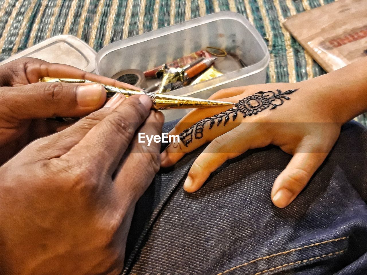 Cropped image of parent applying henna tattoo on child hand at home