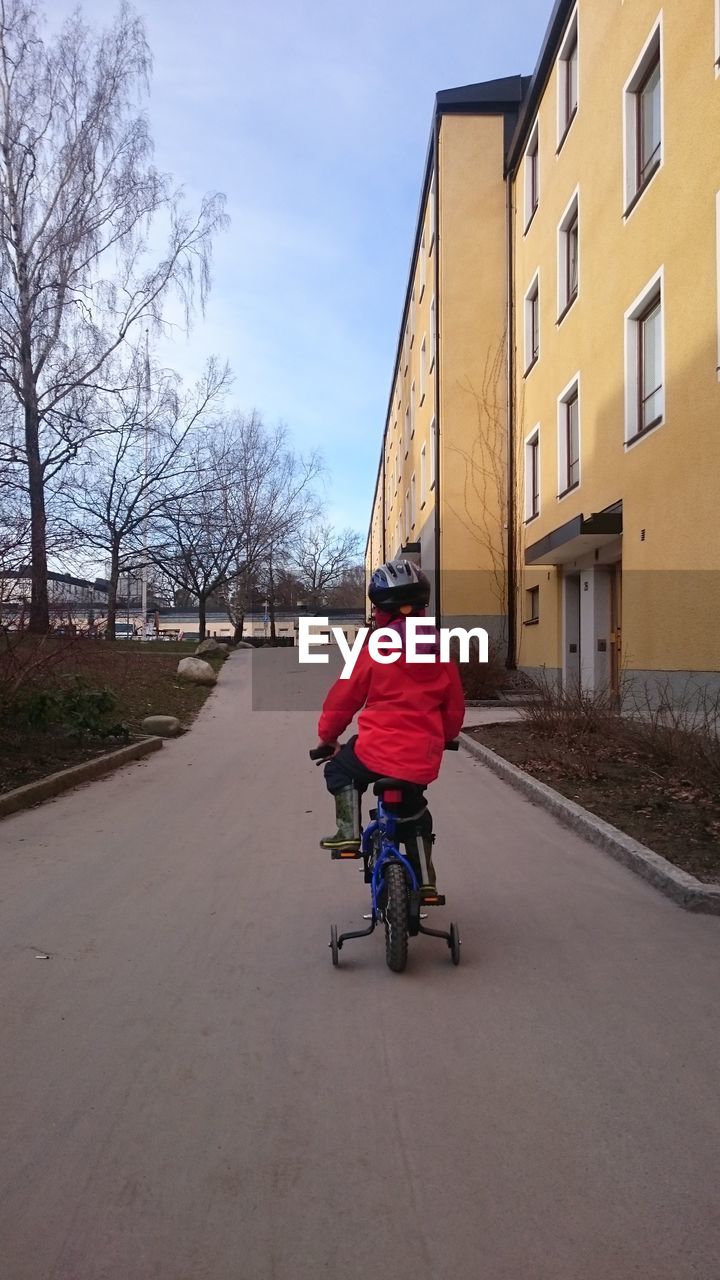 Rear view of boy riding bicycle by building