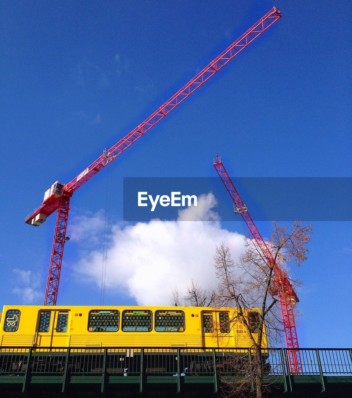 Low angle view of cranes by train on bridge against sky