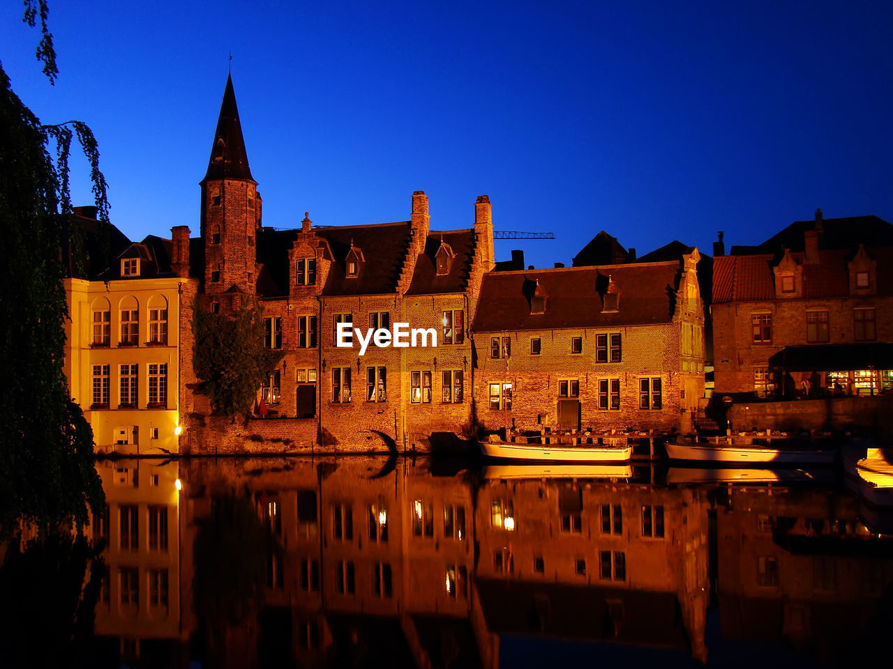 Illuminated buildings by river against clear sky at night