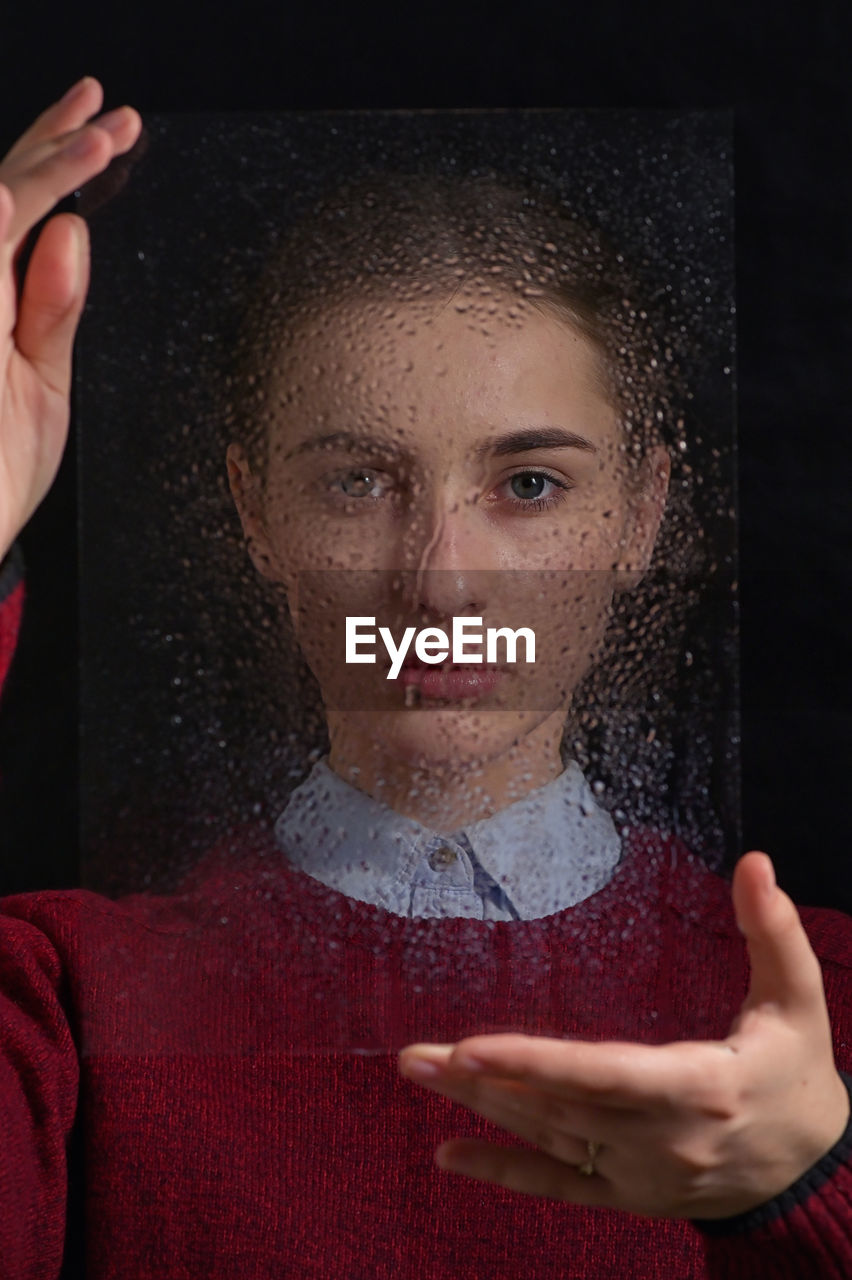 Portrait of woman holding wet glass against black background