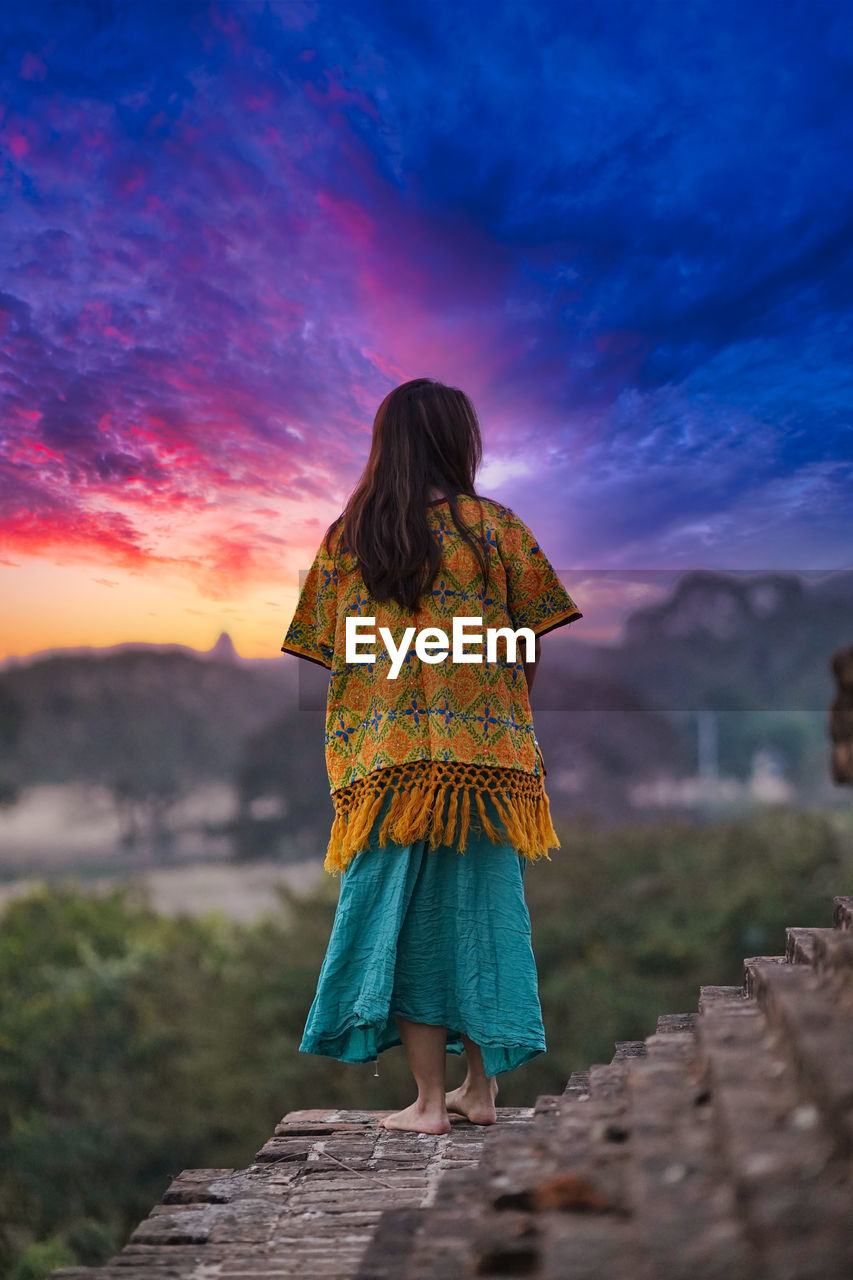 Rear view of woman standing at temple against sky during sunset