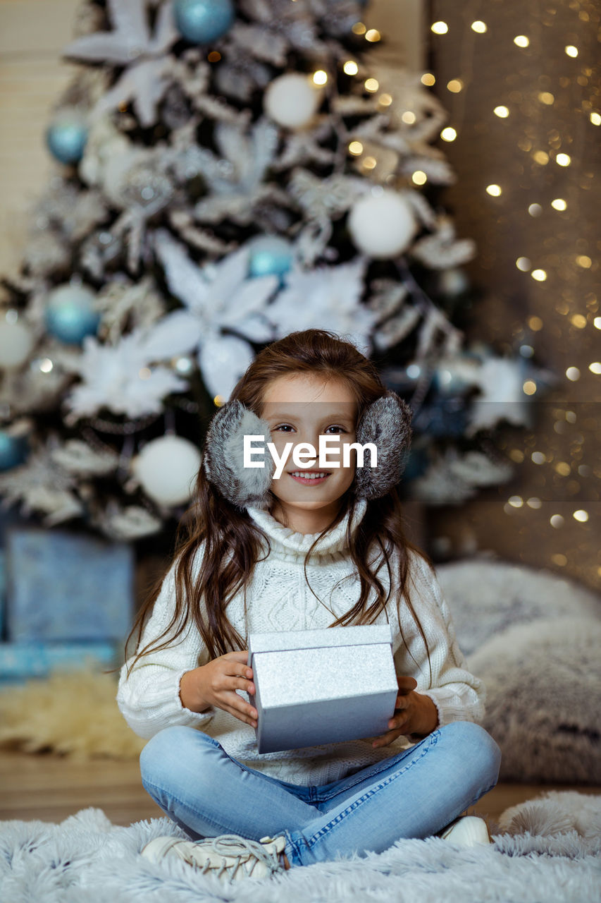 portrait of cute girl looking away while standing against christmas tree