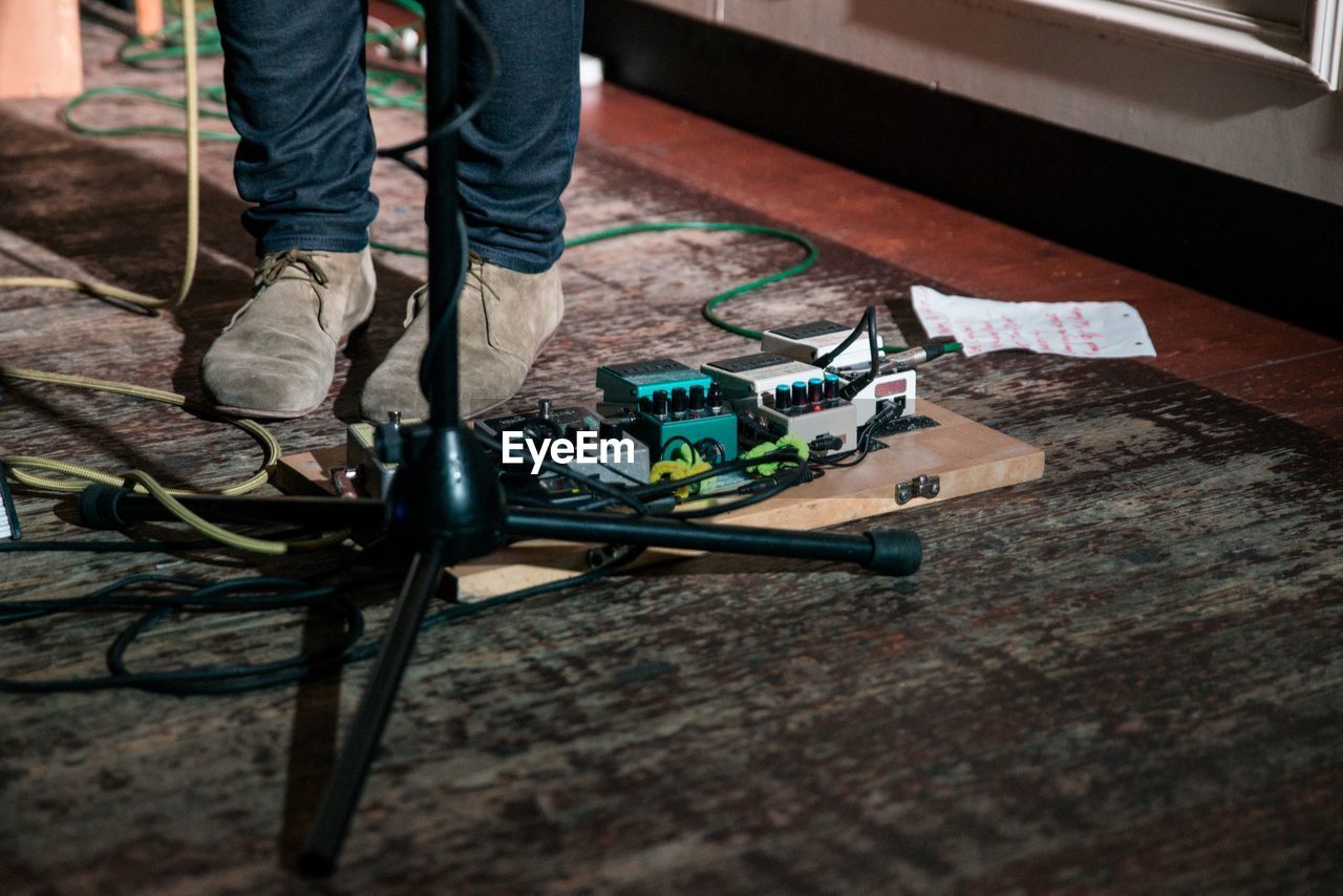 Low section of musician standing by guitar effects pedal on floor