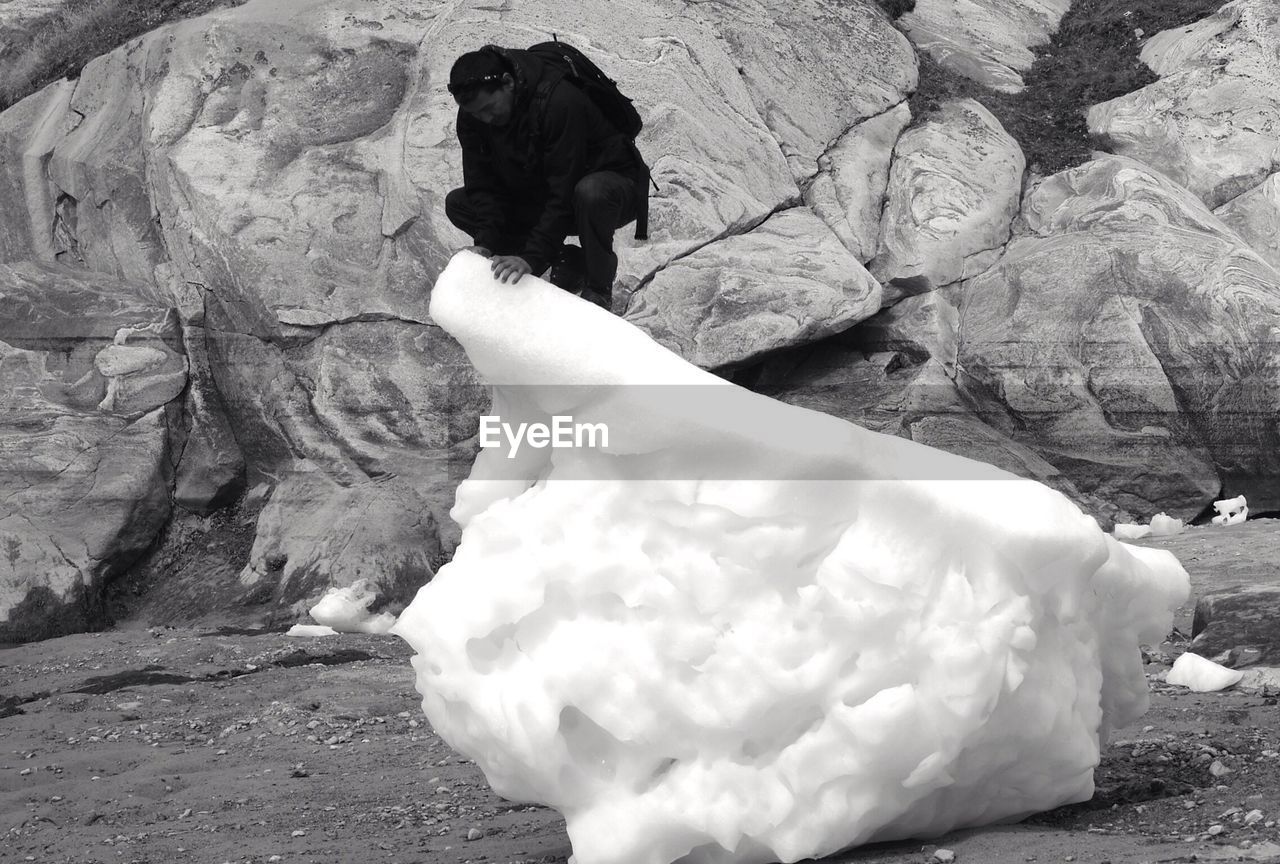 Man crouching on ice against rock formation