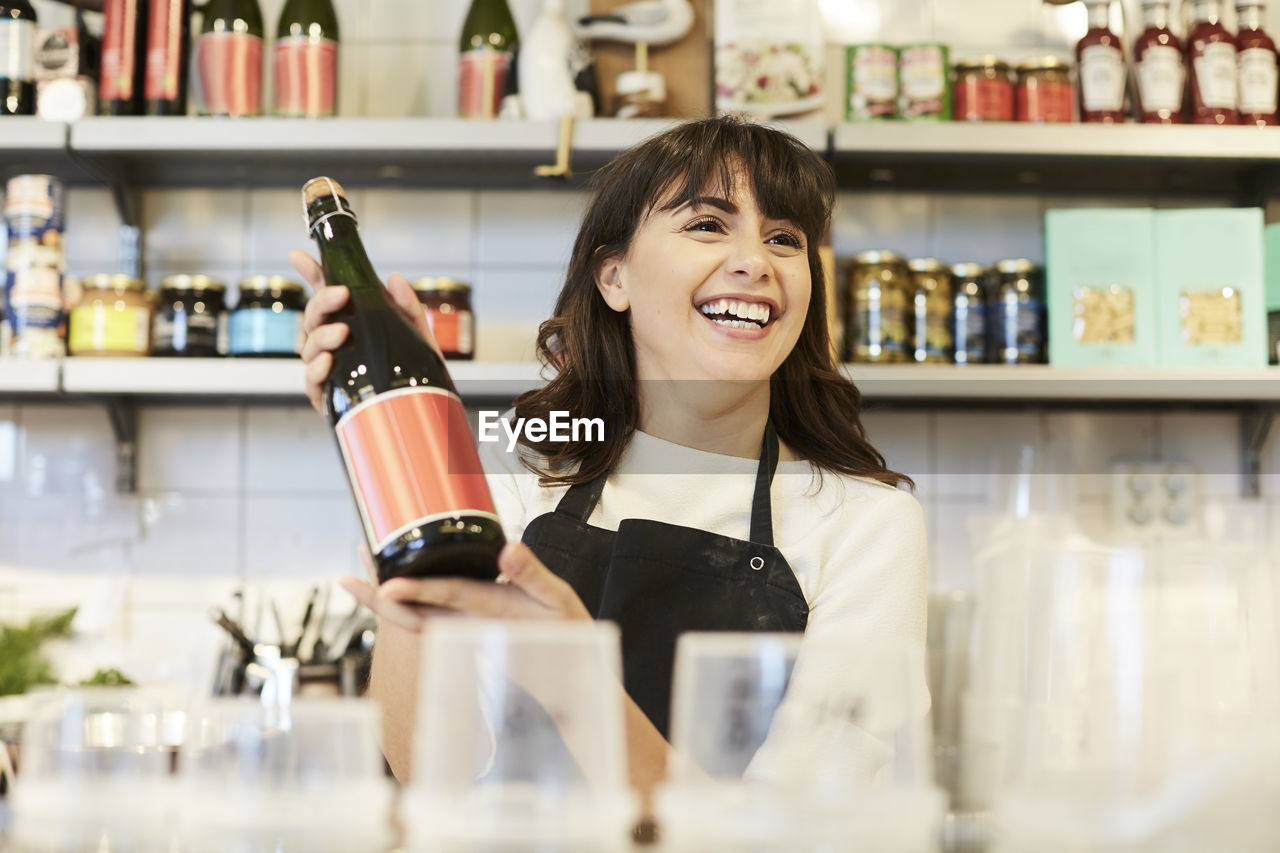 Happy female owner looking away while holding oil bottle at counter in store