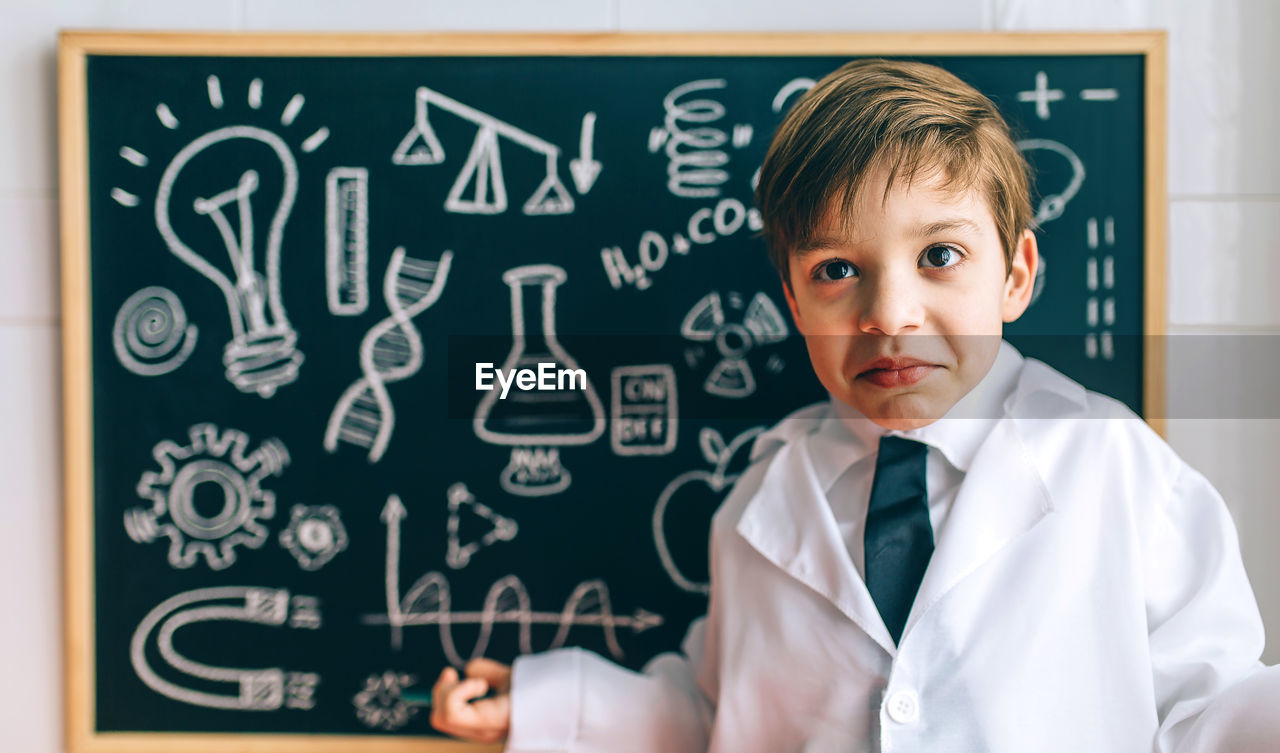 Portrait of cute boy standing against blackboard in classroom