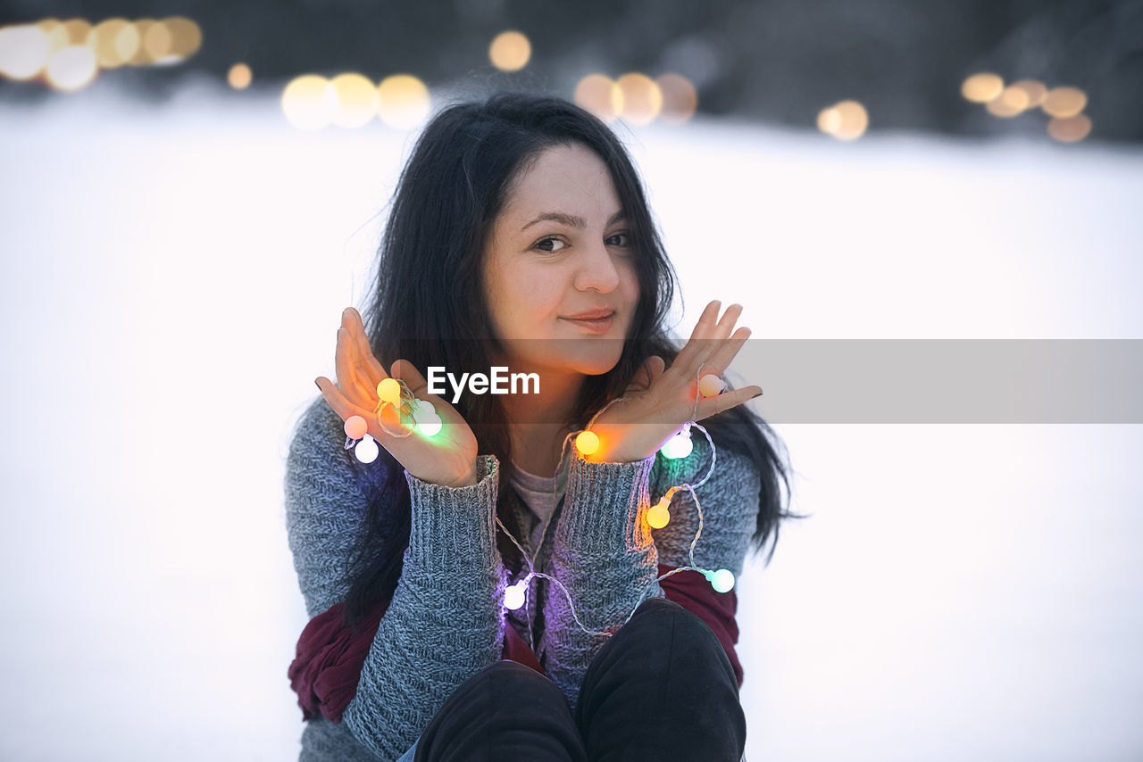 Portrait of young woman holding illuminated christmas lights during sunset