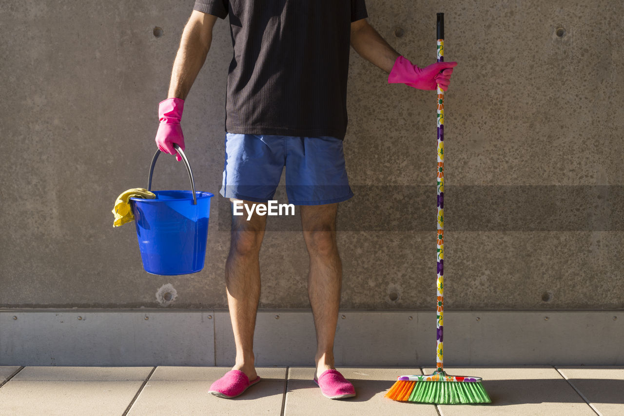 Low section of man with cleaning equipment standing against wall