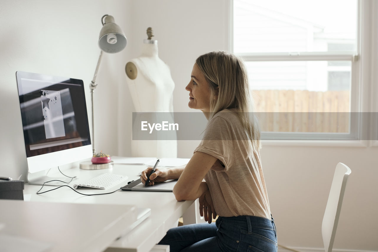 Side view of creative female designer using graphics tablet at home