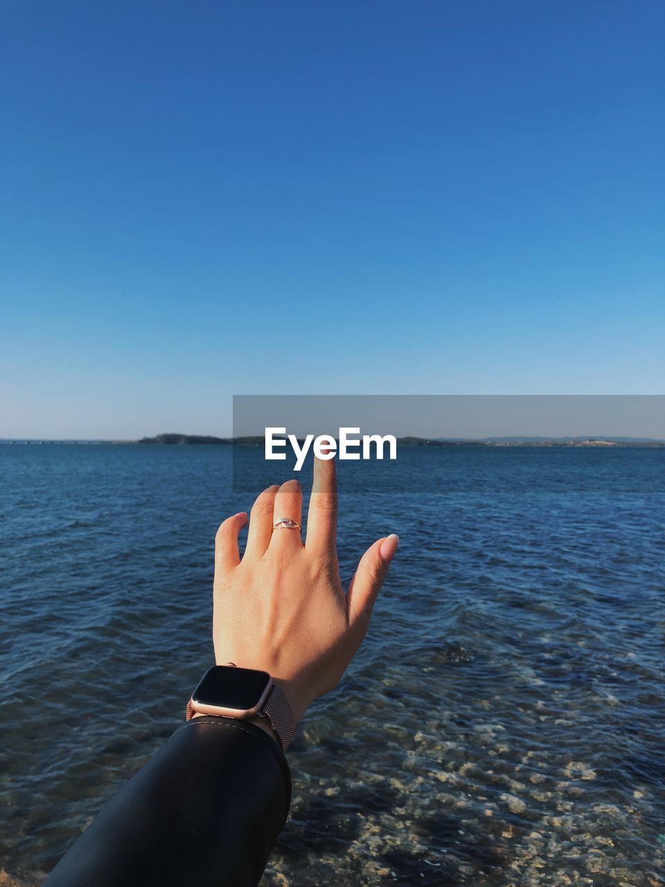 Cropped hand of woman gesturing at beach against clear blue sky