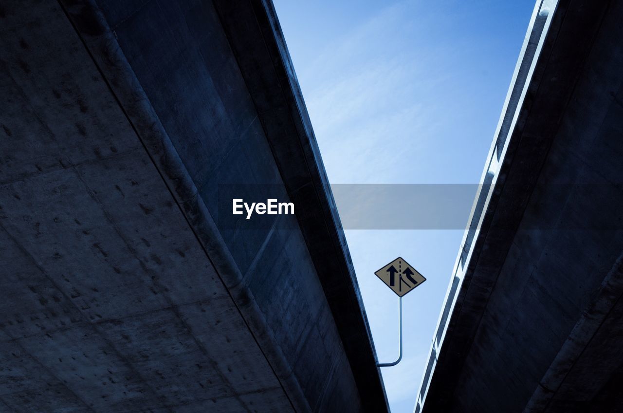 Low angle view of road sign board seen through flyovers against sky