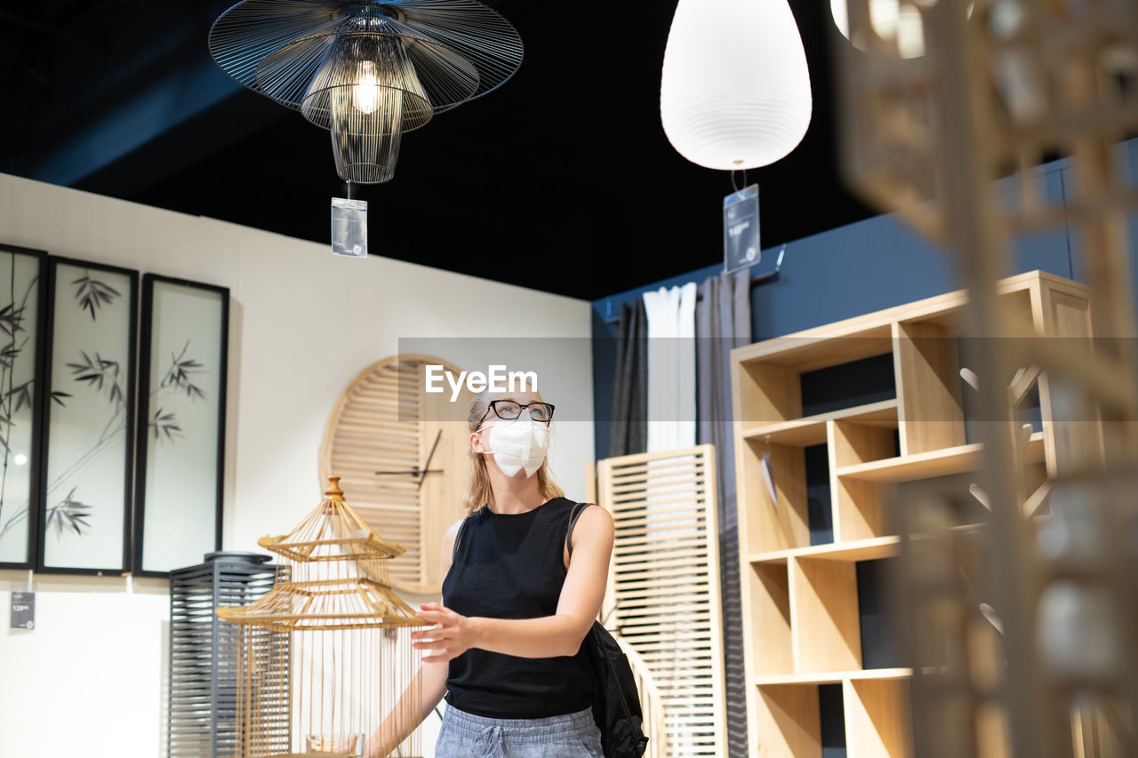 Full length portrait of young woman standing against illuminated lamp