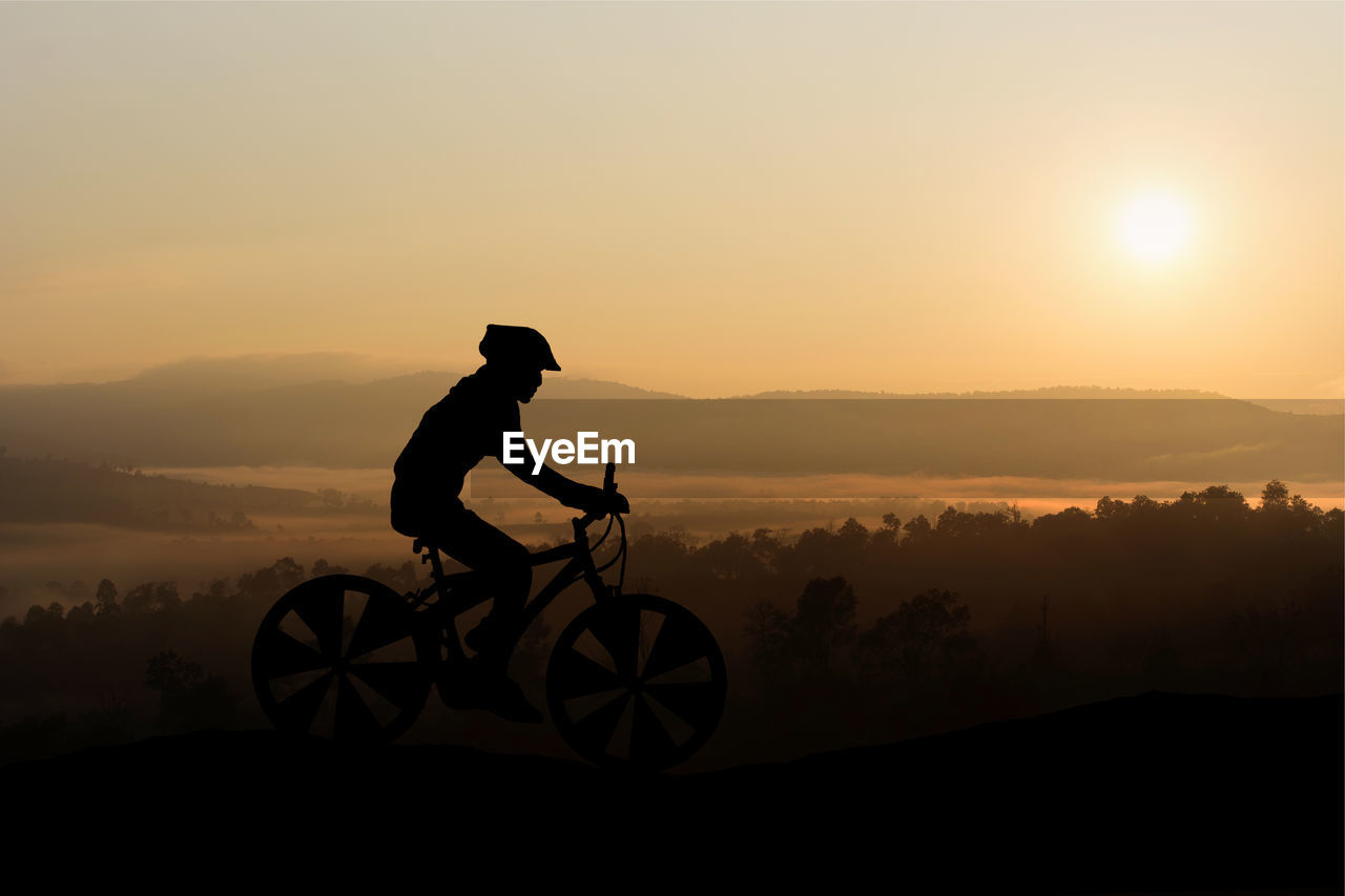 Silhouette man riding bicycle on mountain against sky during sunset