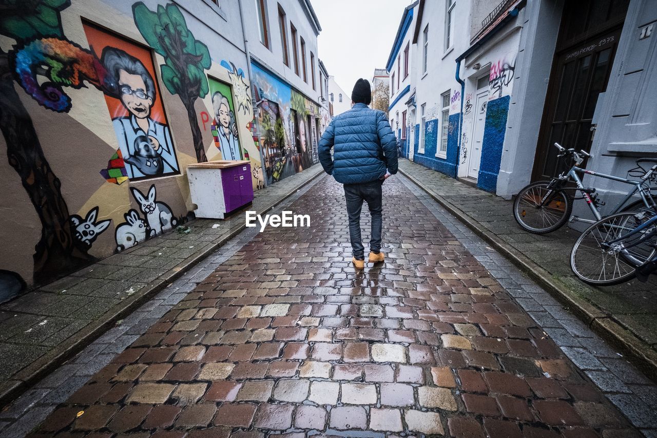 REAR VIEW OF MAN WALKING ON FOOTPATH