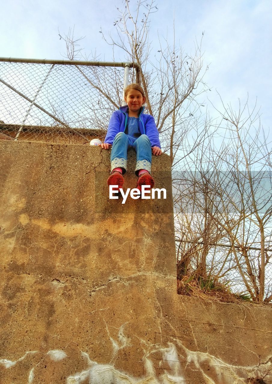 Low angle portrait of girl sitting on retaining wall