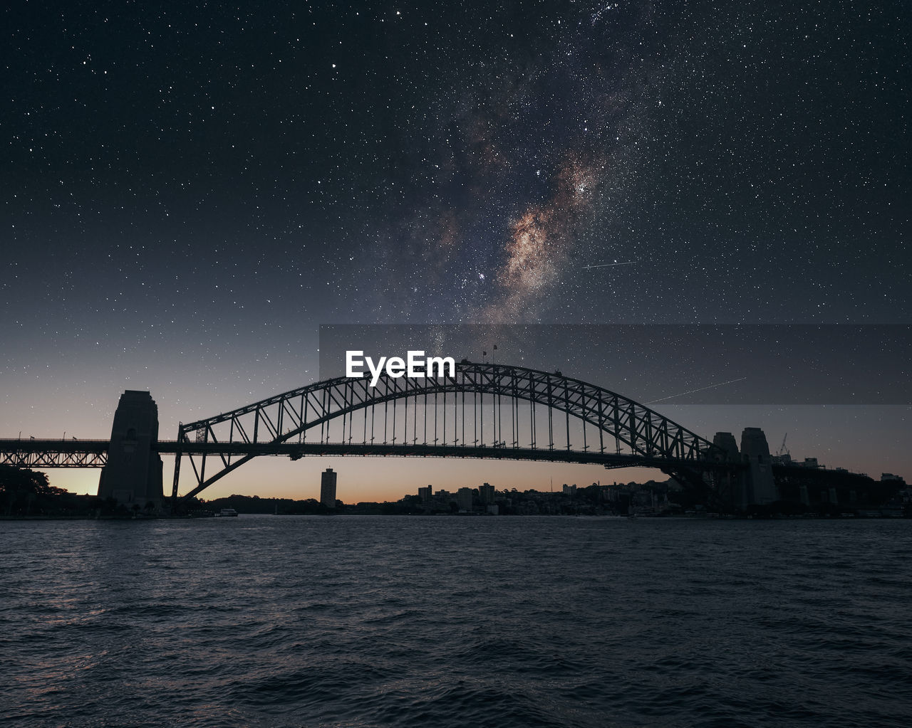 Scenic view of bridge over river against sky in city at night