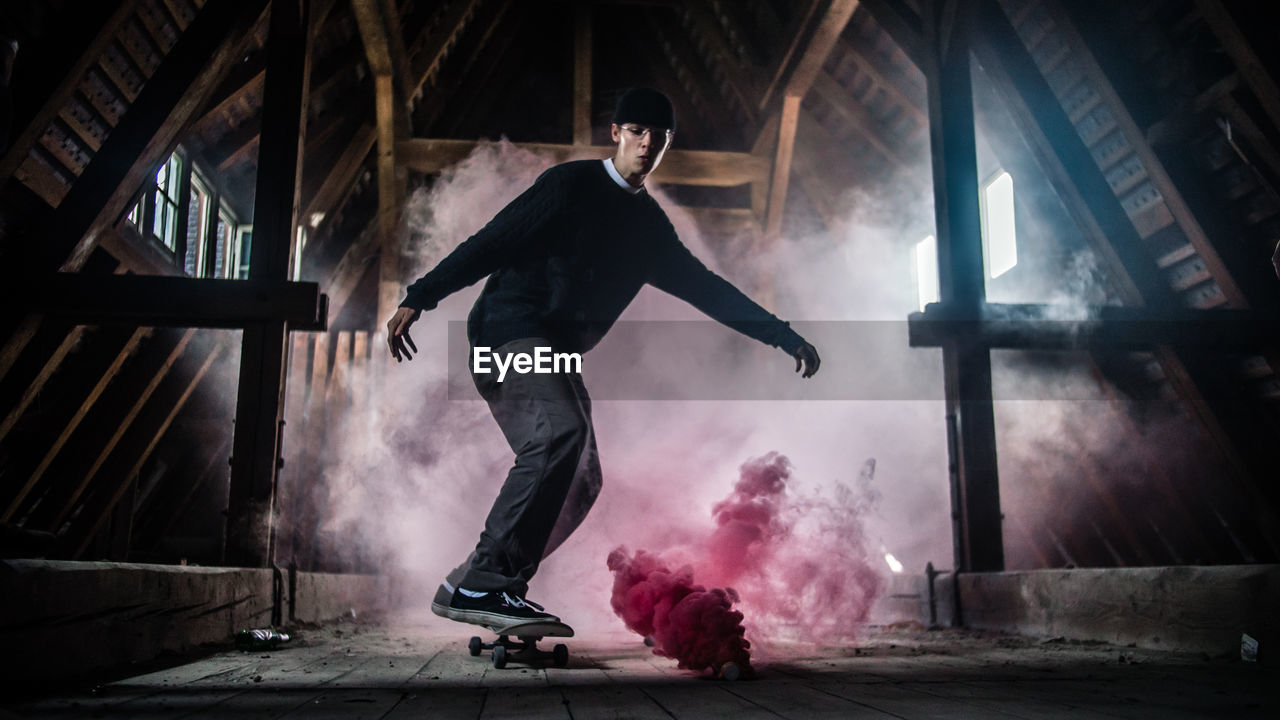 Full length of man skateboarding by red smoke