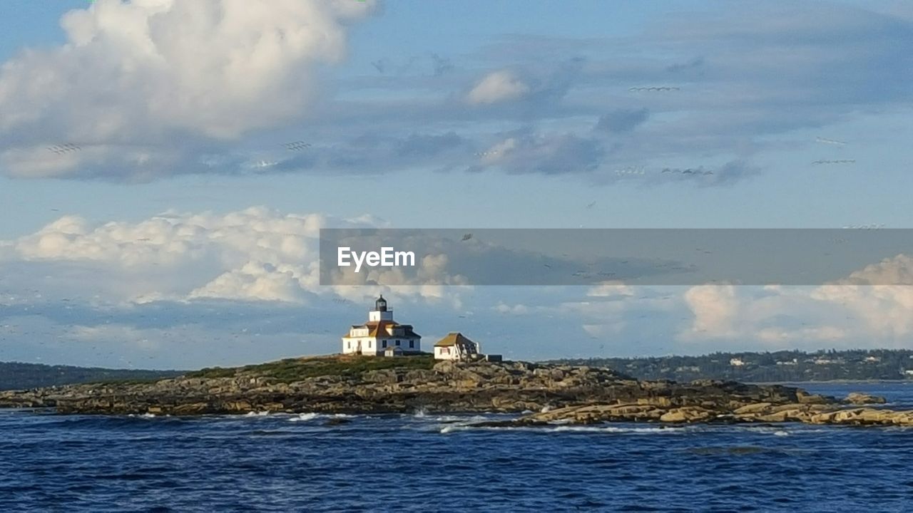 Lighthouse amidst sea against cloudy sky