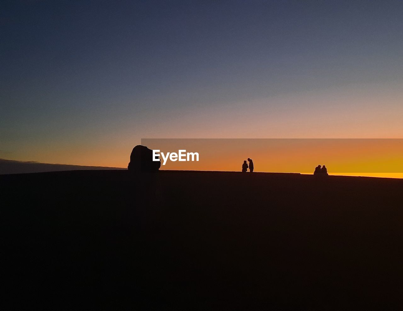 silhouette people walking on rock against sky during sunset