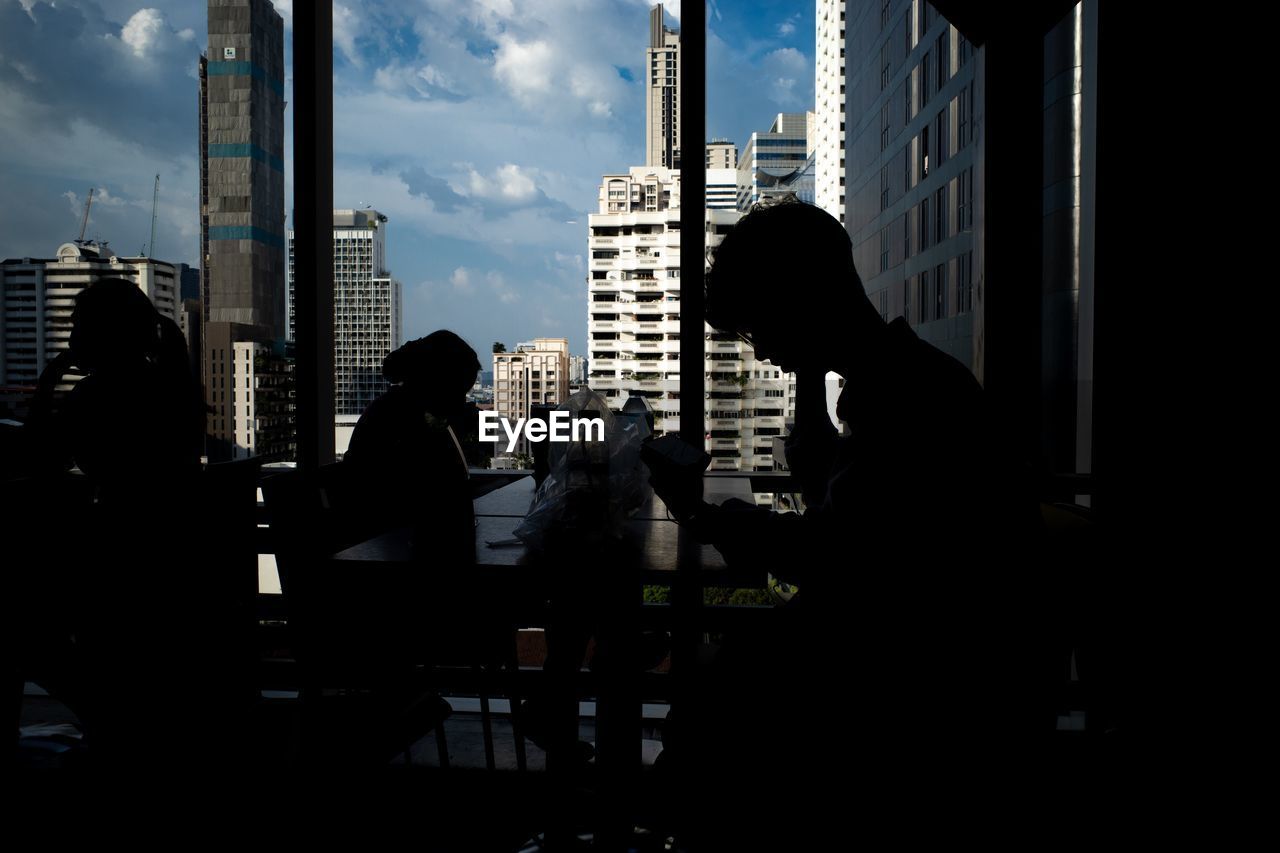 SILHOUETTE PEOPLE SITTING ON TABLE BY BUILDINGS AGAINST CITY