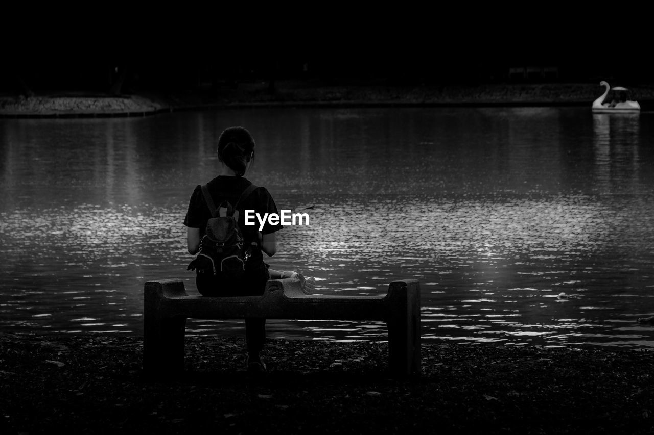 REAR VIEW OF MAN SITTING ON BENCH AGAINST LAKE