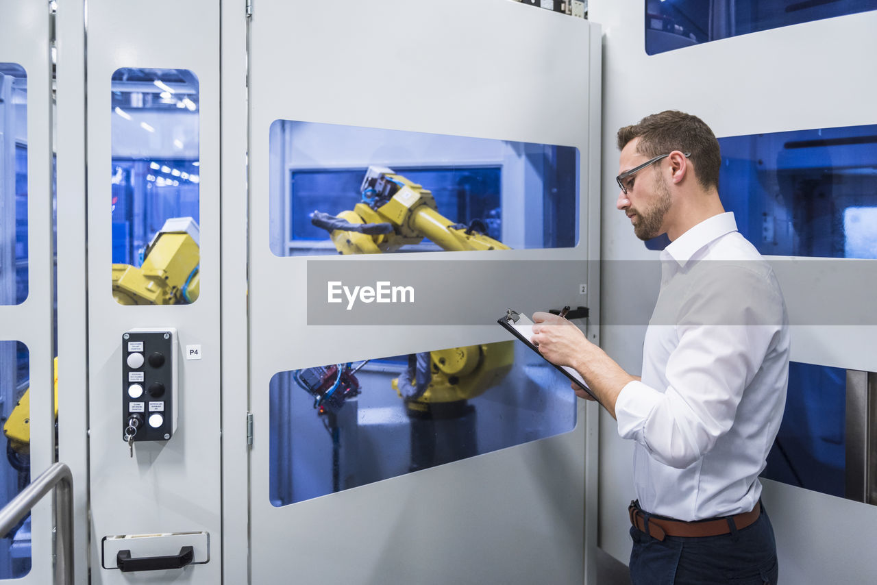 Man taking notes at robotics machine in factory shop floor