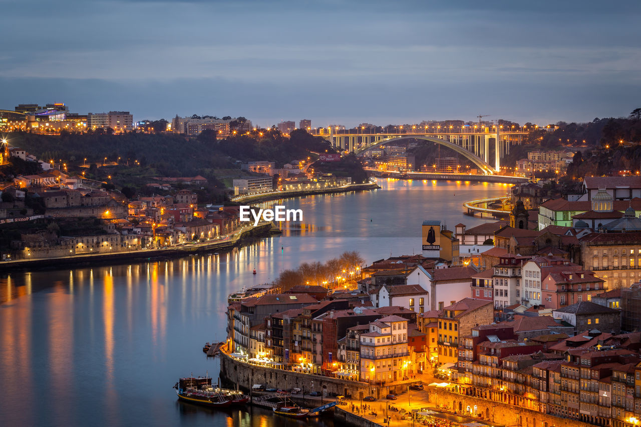 HIGH ANGLE VIEW OF ILLUMINATED BRIDGE OVER RIVER BY BUILDINGS IN CITY