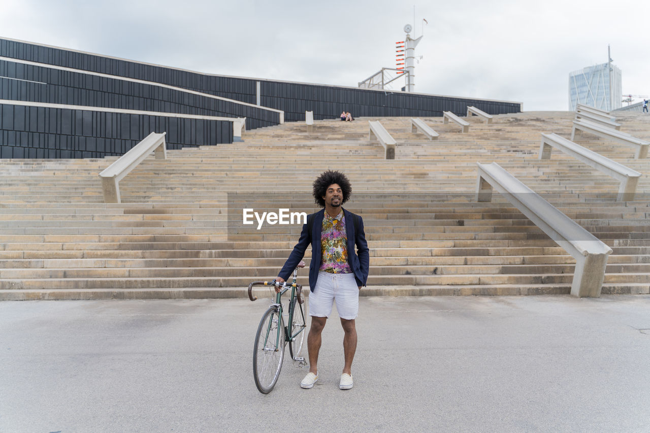 Stylish man with bicycle standing at stairs