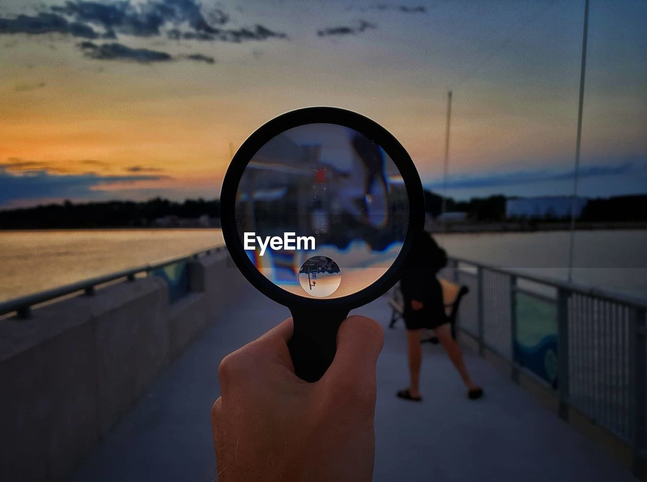 Close-up of hand holding magnifying glass against sky