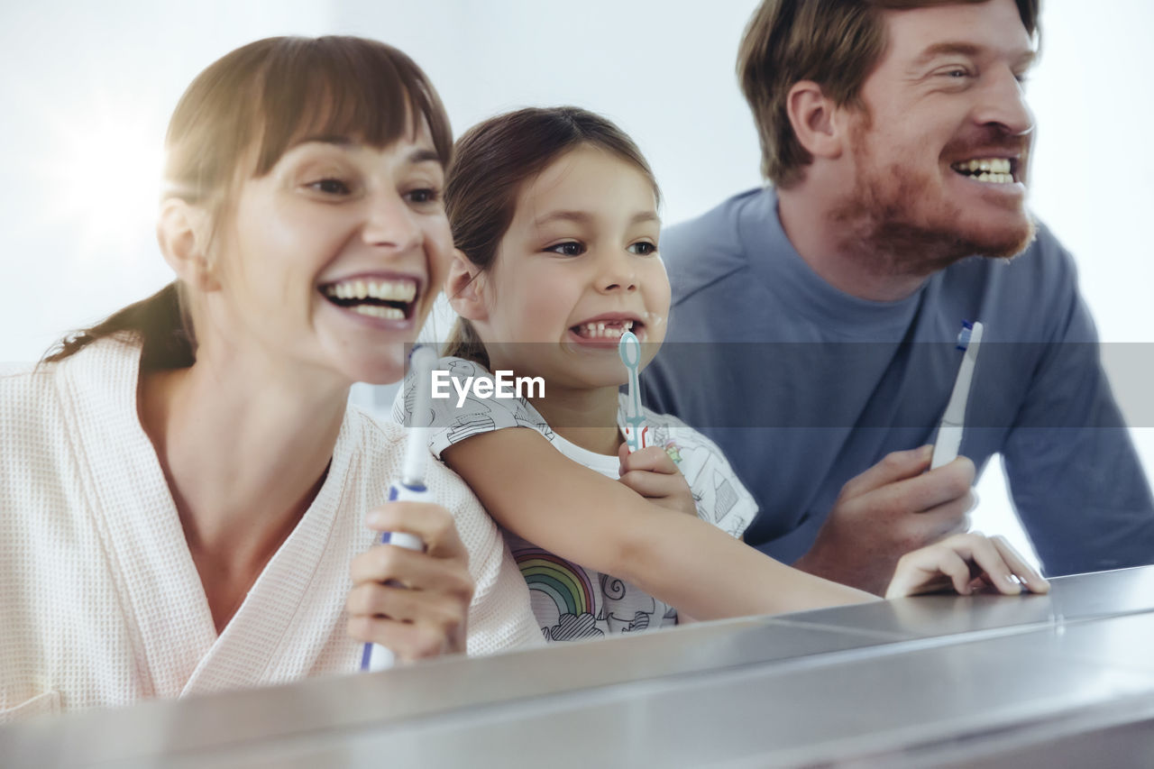 Family of three brushing their teeth in front of big mirror