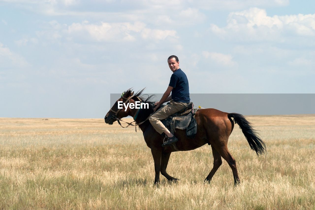 Portrait of man riding horse on field against cloudy sky