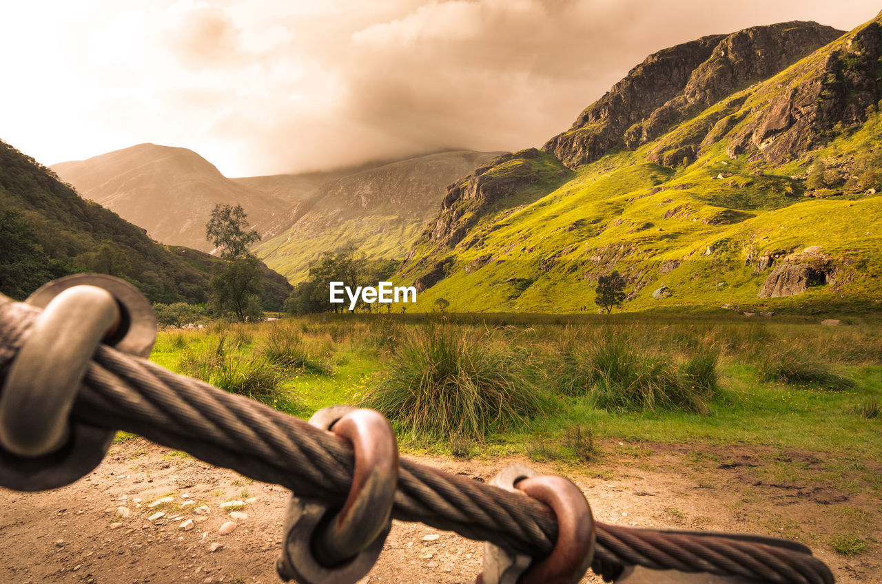 FENCE ON FIELD AGAINST MOUNTAINS