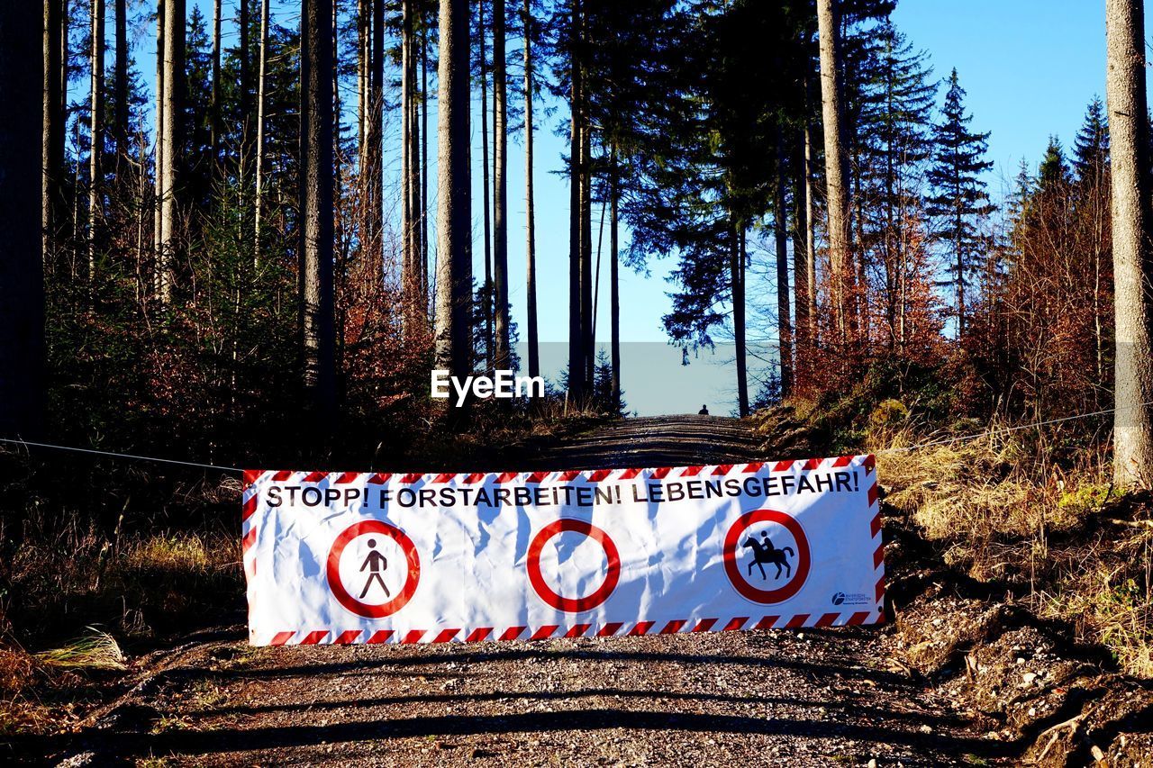 Sign banner on dirt road amidst trees