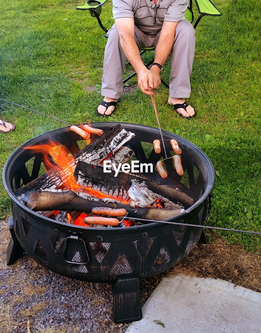 Low section of man roasting sausages over fire pit