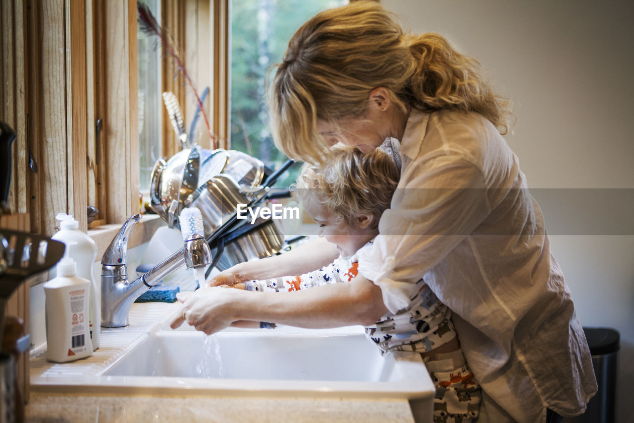 Mother assisting son in washing hands at kitchen sink