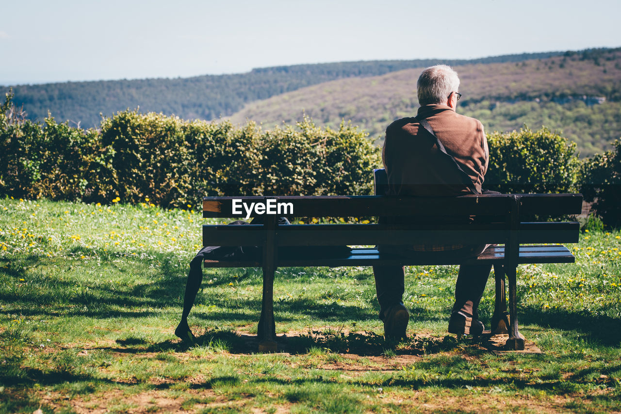 Rear view of senior man sitting on bench against mountain