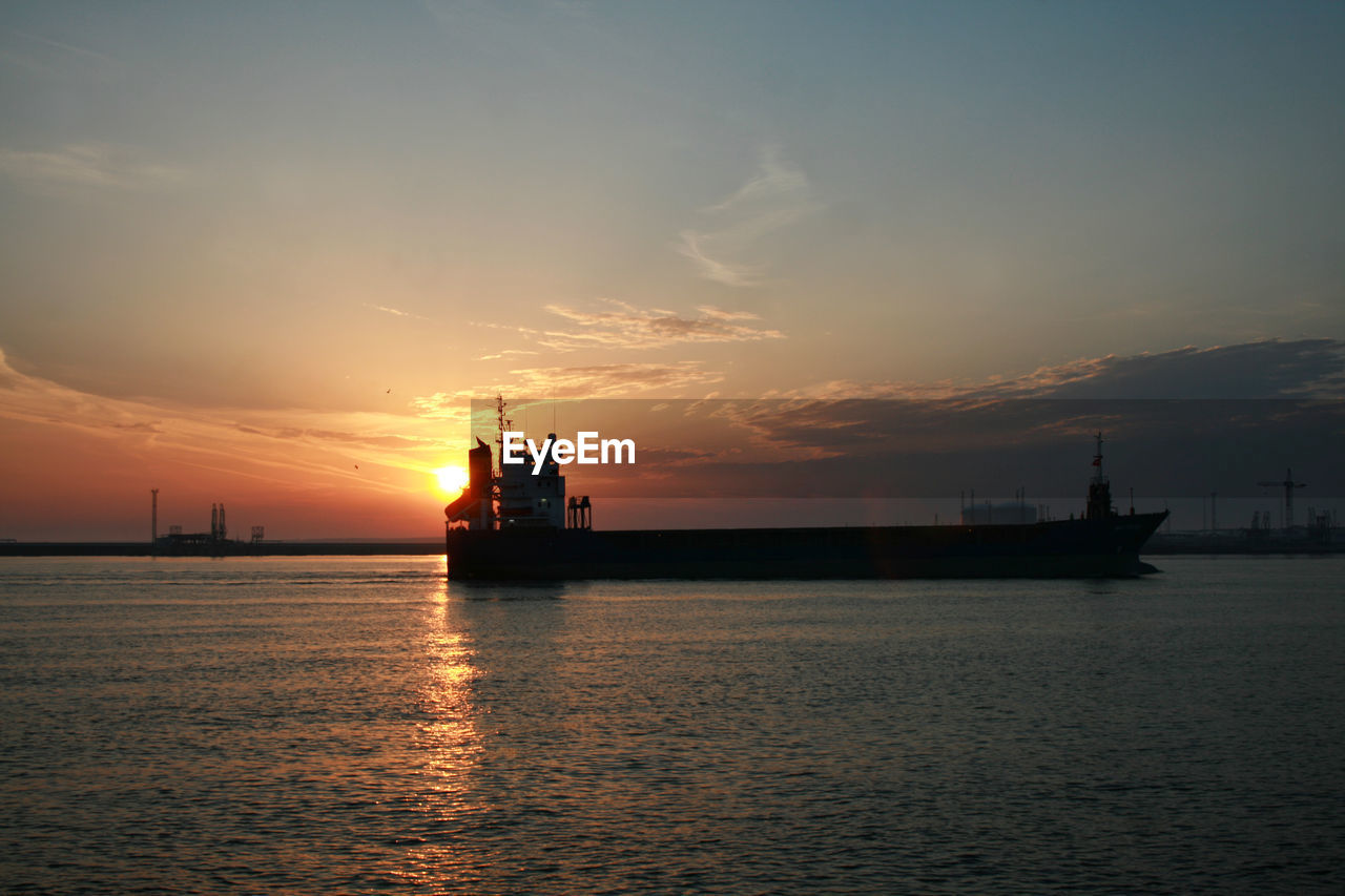 Scenic view of container ship entering harbor during sunrise