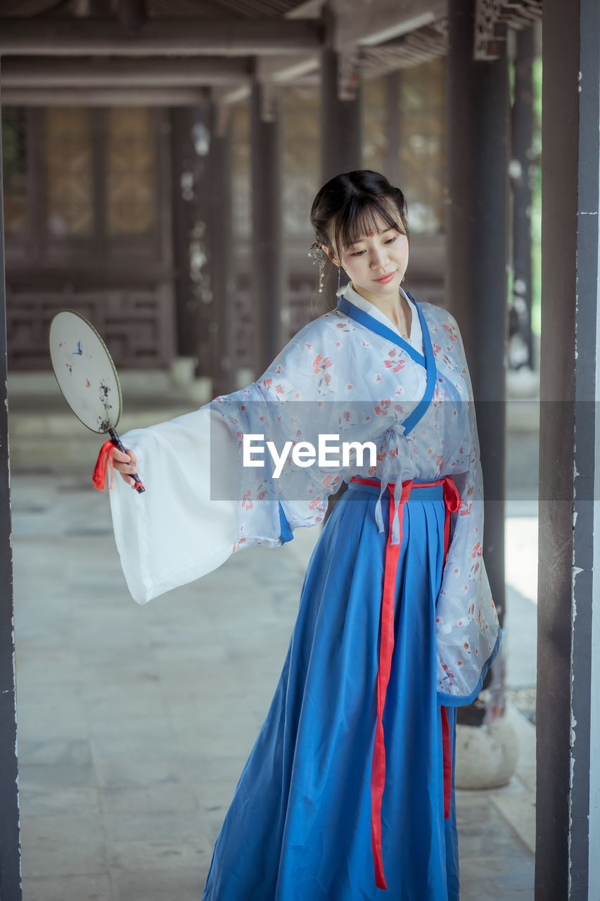 Woman in kimono holding hand fan at corridor