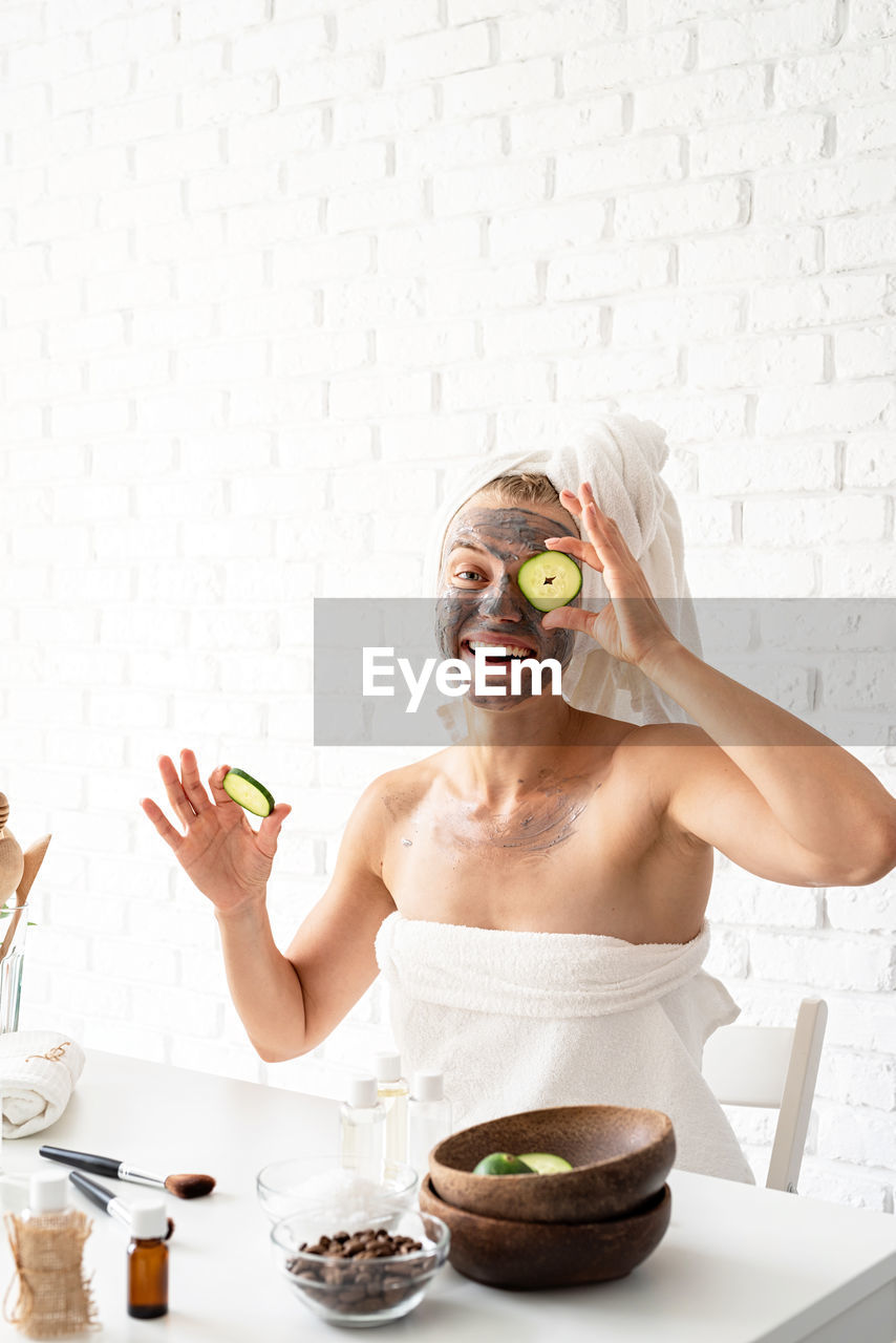 Young woman wearing white towels applying spa facial mask on her face with a cosmetic brush