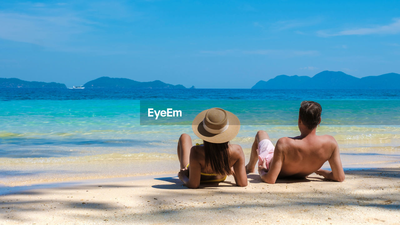 rear view of woman sitting on beach against sky