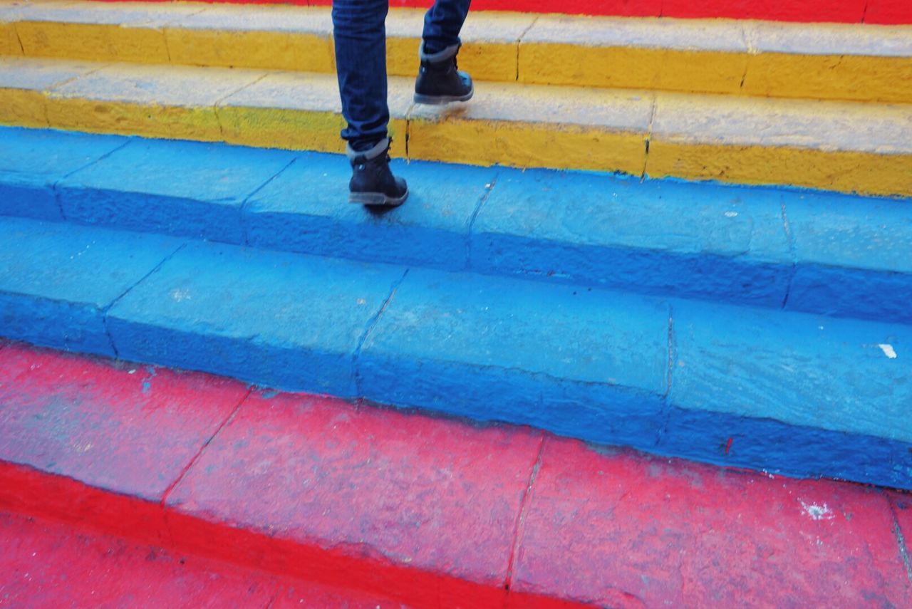 Low section of person climbing multi colored staircase