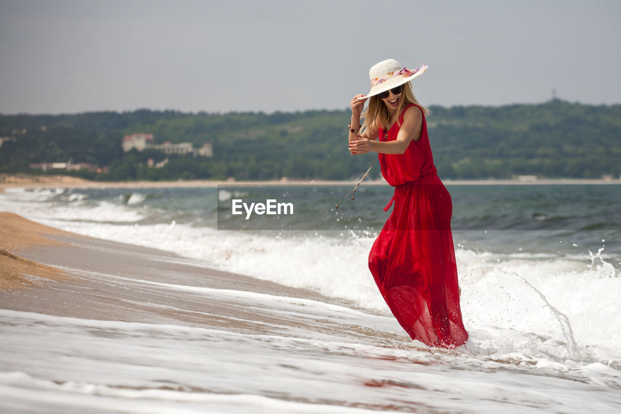 Woman wearing hat running at shore against sky