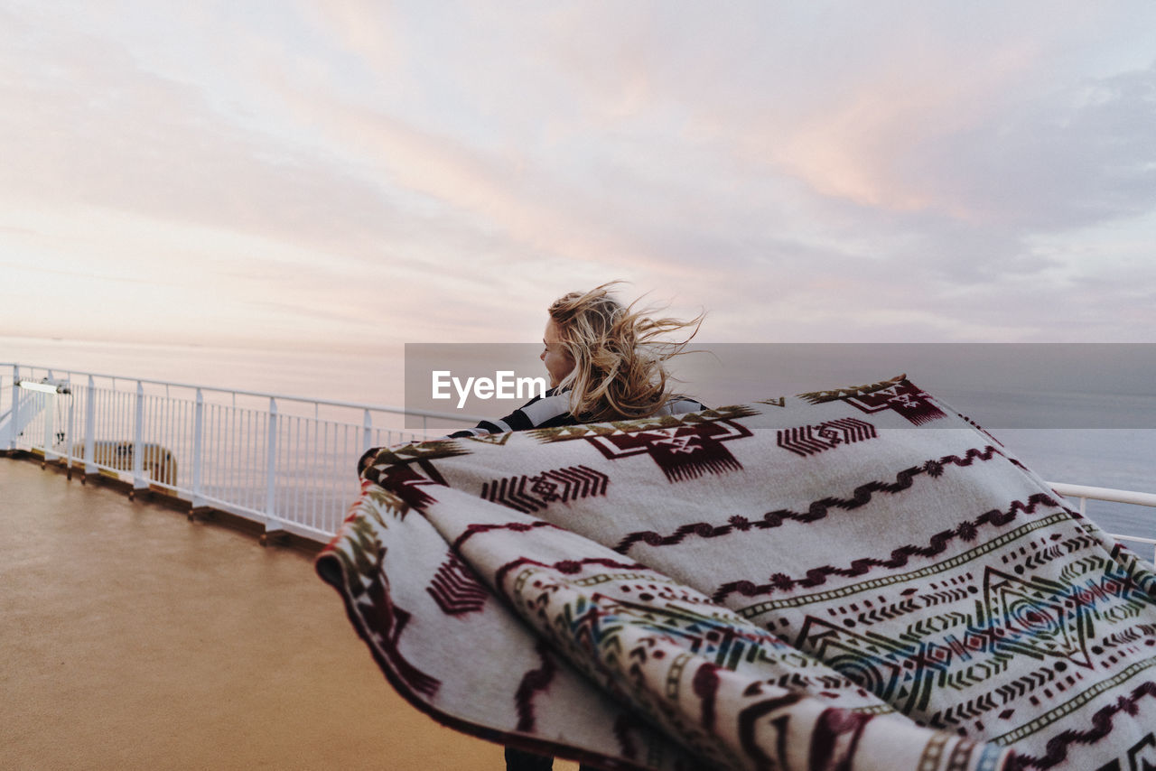 WOMAN STANDING BY RAILING AGAINST SEA