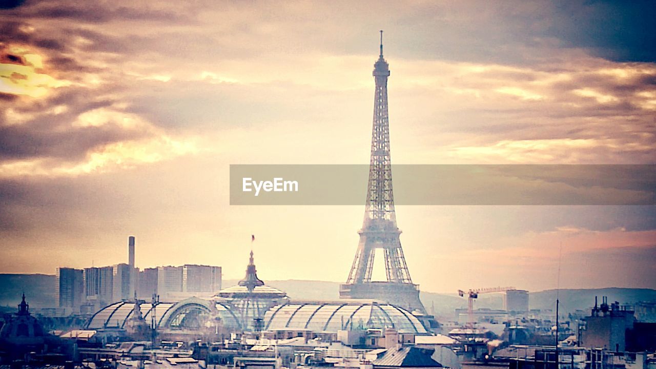 Eiffel tower and cityscape against cloudy sky at sunset