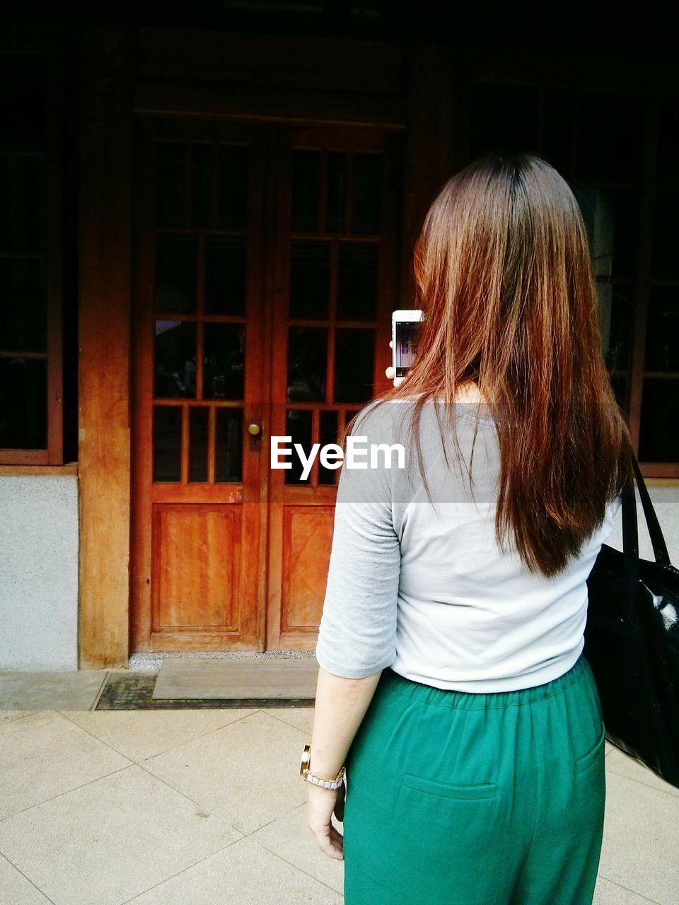 Rear view of woman holding smart phone and standing on floor