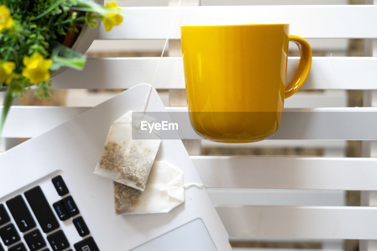 Tea bags next to a laptop and a yellow cup.