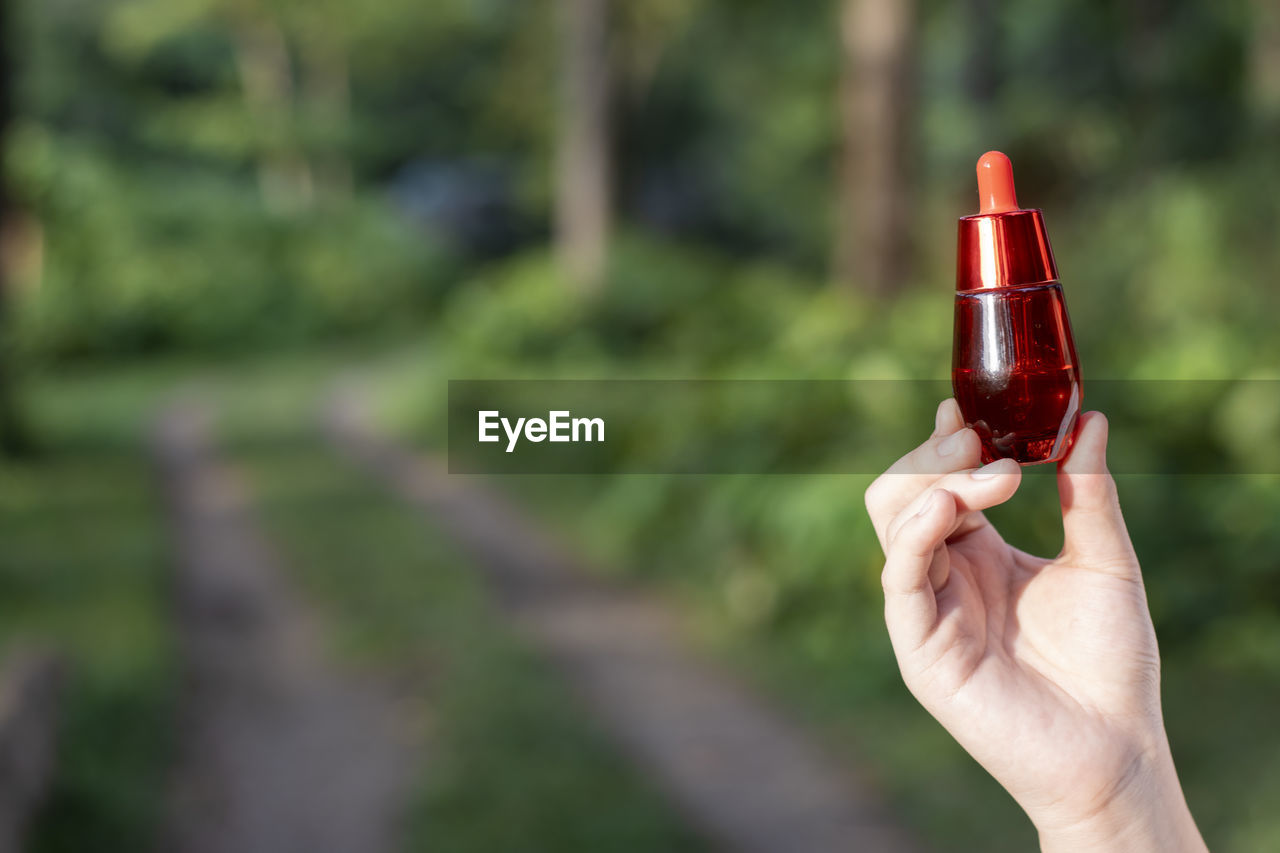 Selective focus red facial serum bottle in asian woman's hand nature background 