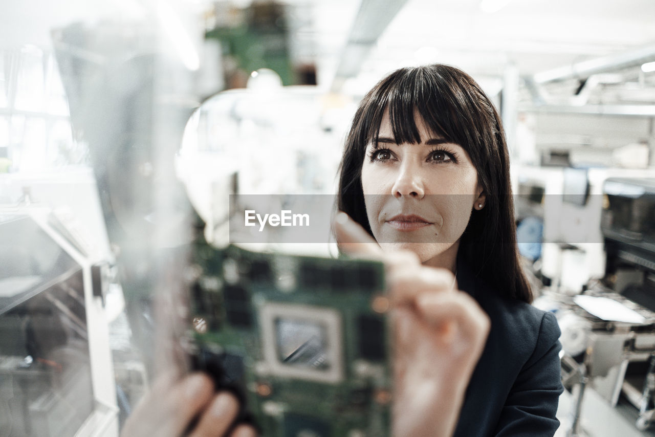 Confident female professional investigating while looking at circuit board in industry